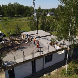 MaG Inwest - Wylewanie betonu na strop domu jednorodzinnego z betonu komórkowego; widoczni robotnicy w kamizelkach odblaskowych i kaskach, pompa do betonu, szalunki i zbrojenie.