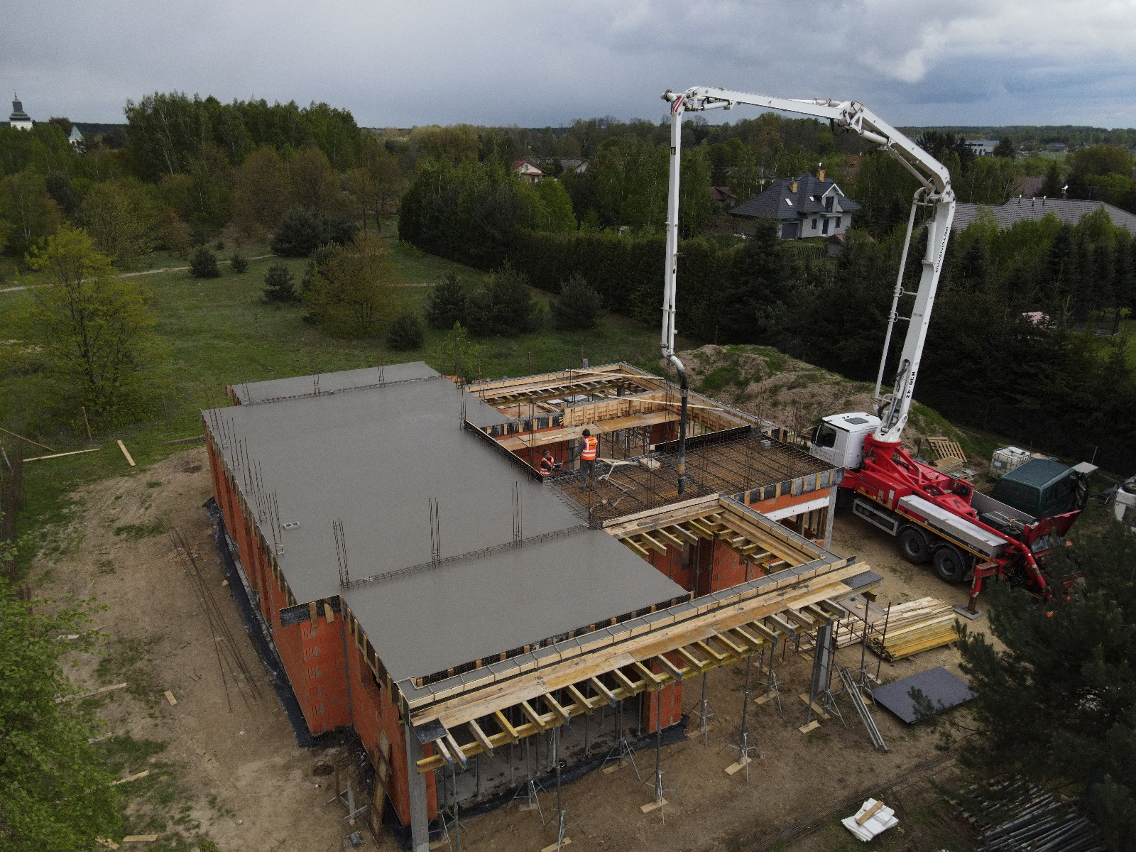 Wylewanie betonu na strop domu jednorodzinnego w stanie surowym otwartym z użyciem pompy do betonu, widok z drona na plac budowy.