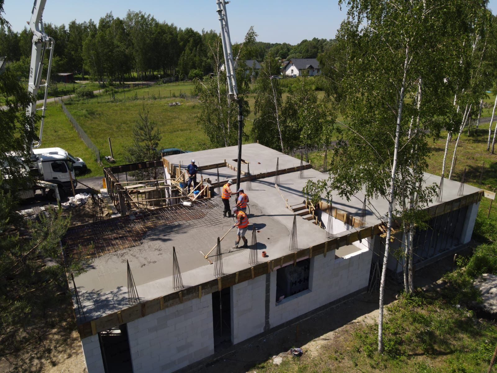 Wylewanie betonu na strop domu jednorodzinnego z betonu komórkowego; widoczni robotnicy w kamizelkach odblaskowych i kaskach, pompa do betonu, szalunki i zbrojenie.
