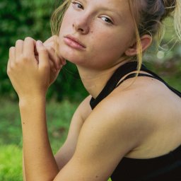 Adela Mróz - Portret młodej kobiety z piegami, włosy upięte w luźny kok, spojrzenie w obiektyw, tło z zieleni