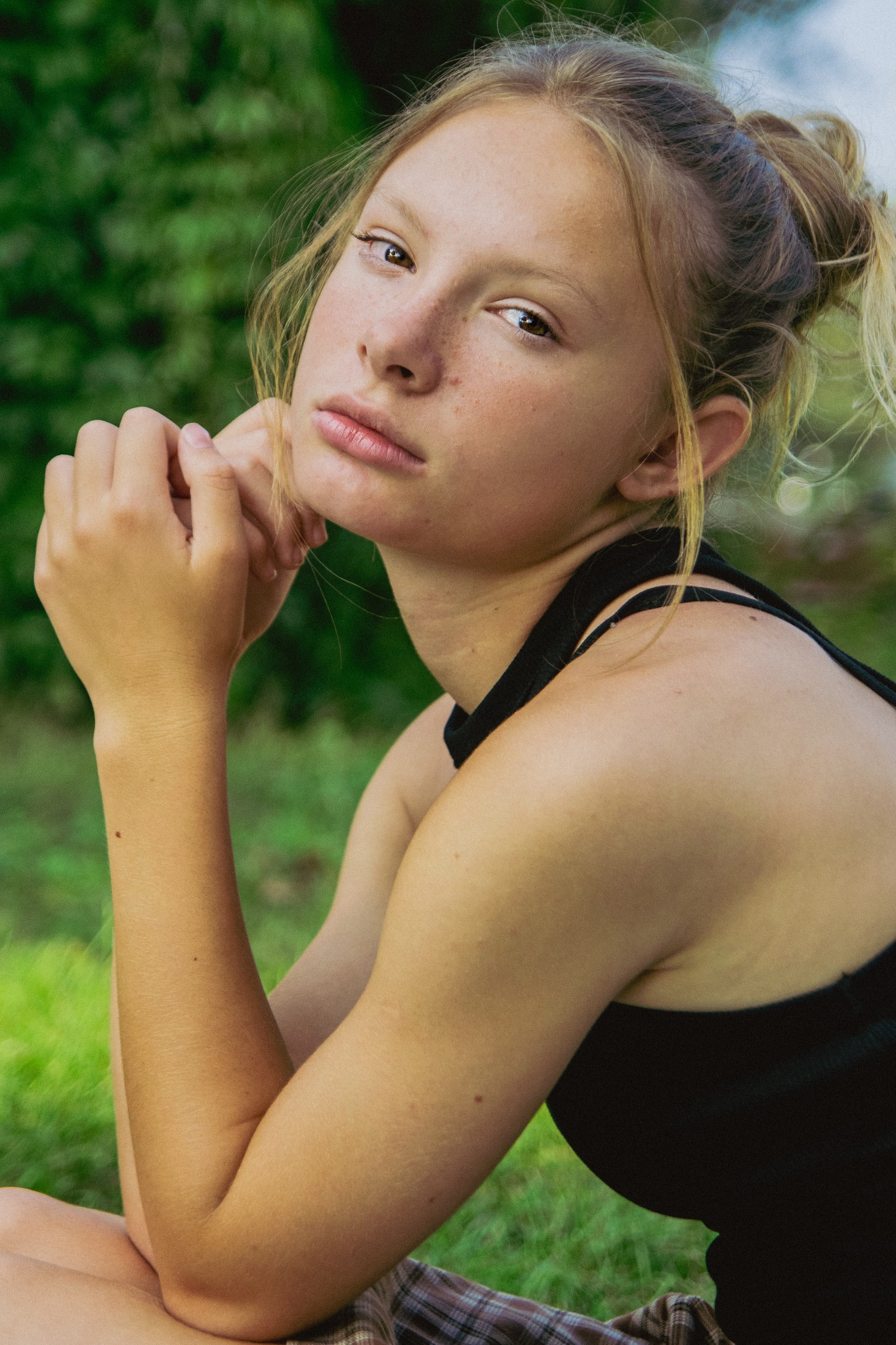 Portret młodej kobiety z piegami, włosy upięte w luźny kok, spojrzenie w obiektyw, tło z zieleni