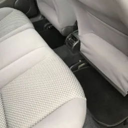 Wnętrze samochodu z jasną, wzorzystą tapicerką tylnych siedzeń i czarnymi dywanikami, widoczne detale mocowania siedzeń.