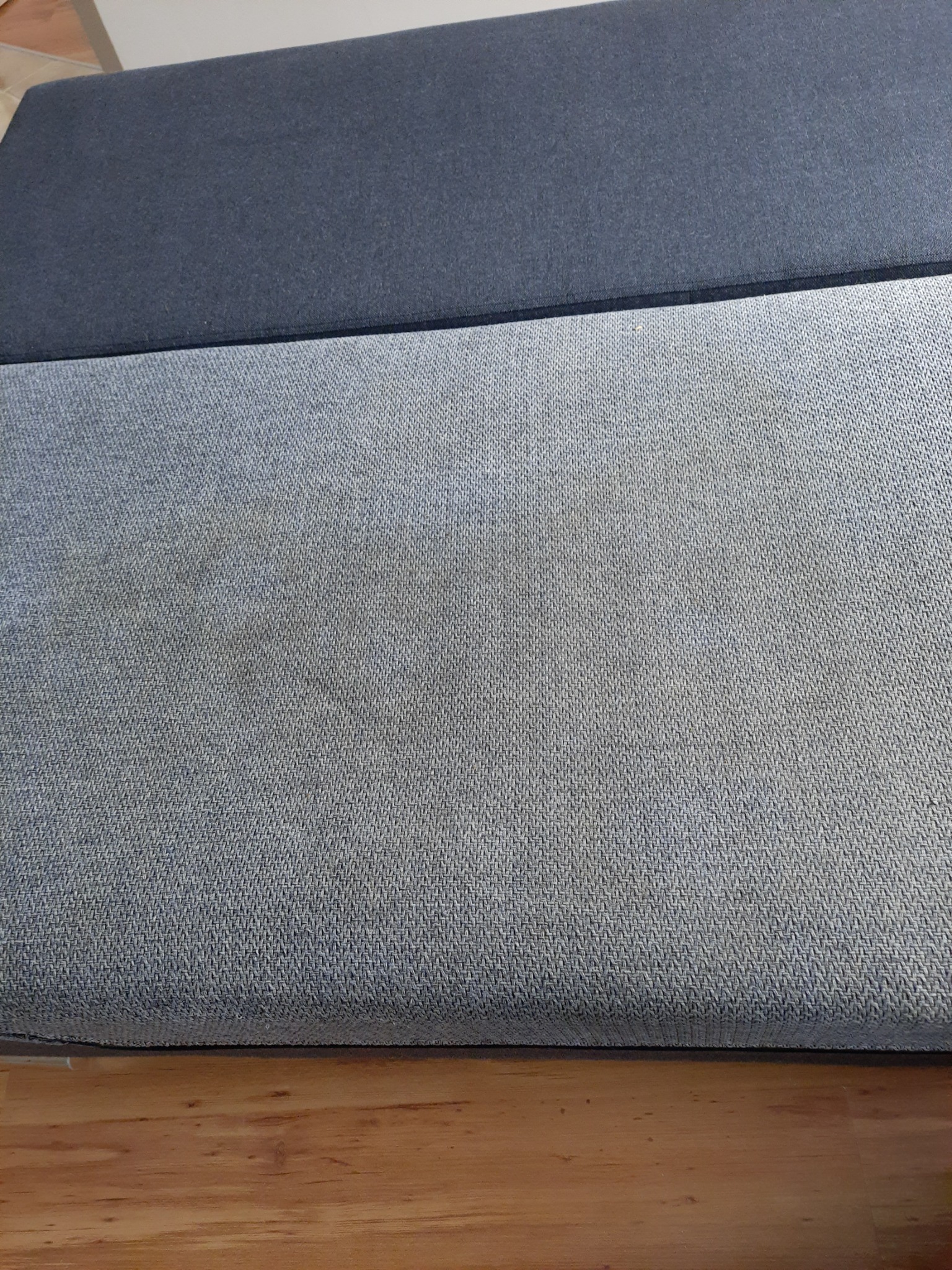 Fragment dwukolorowej tapicerki z widocznymi plamami na jaśniejszej części, leżącej na drewnianej podłodze.