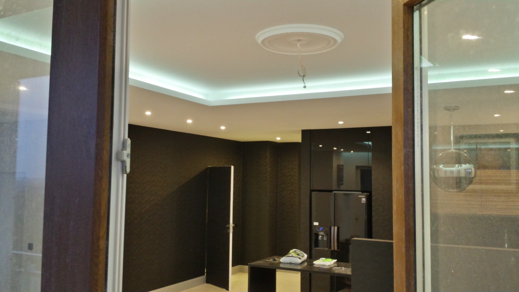 Nowoczesne wnętrze biura z czarnymi ścianami, oświetleniem LED na suficie i widoczną instalacją elektryczną w miejscu na lampę. Widok przez otwarte okno z drewnianą ramą.