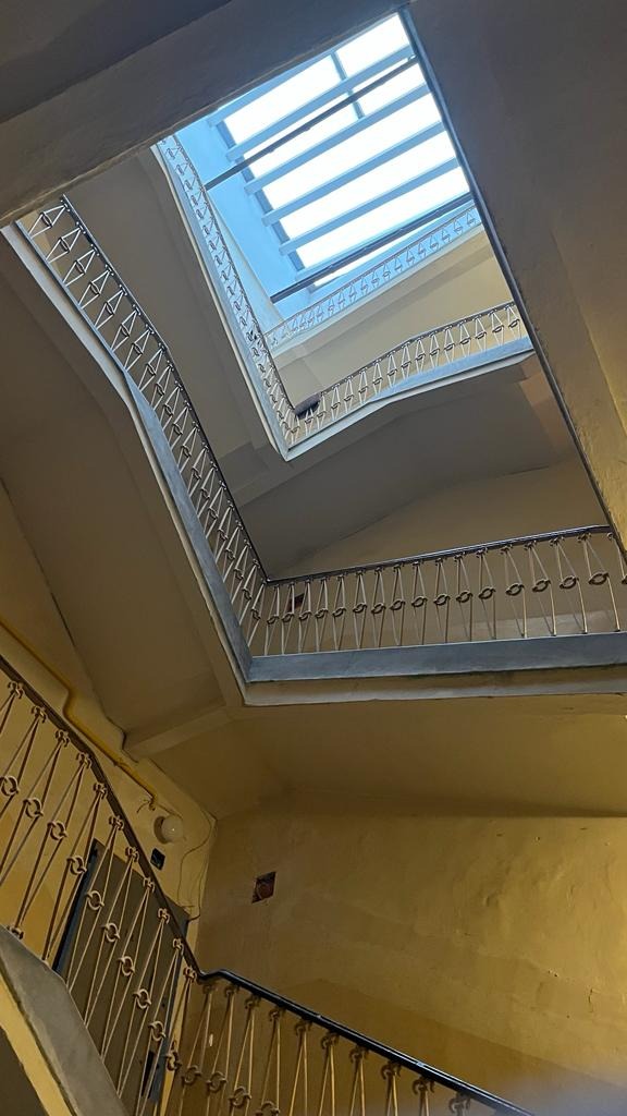 Klatka schodowa w kamienicy z widokiem na świetlik dachowy, malowane na żółto ściany, metalowe balustrady z ornamentami.