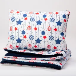 Stos pościeli: poduszka i kołdra z białej tkaniny w niebieskie gwiazdy, czerwone gwiazdki i bombki na białym tle, dolna warstwa z granatowego pluszu.