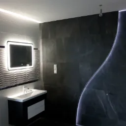 Nowoczesna łazienka z czarno-białymi płytkami, podświetlanym lustrem i dekoracyjnym oświetleniem LED wzdłuż ściany prysznicowej, oraz wisząca umywalka z szafką.