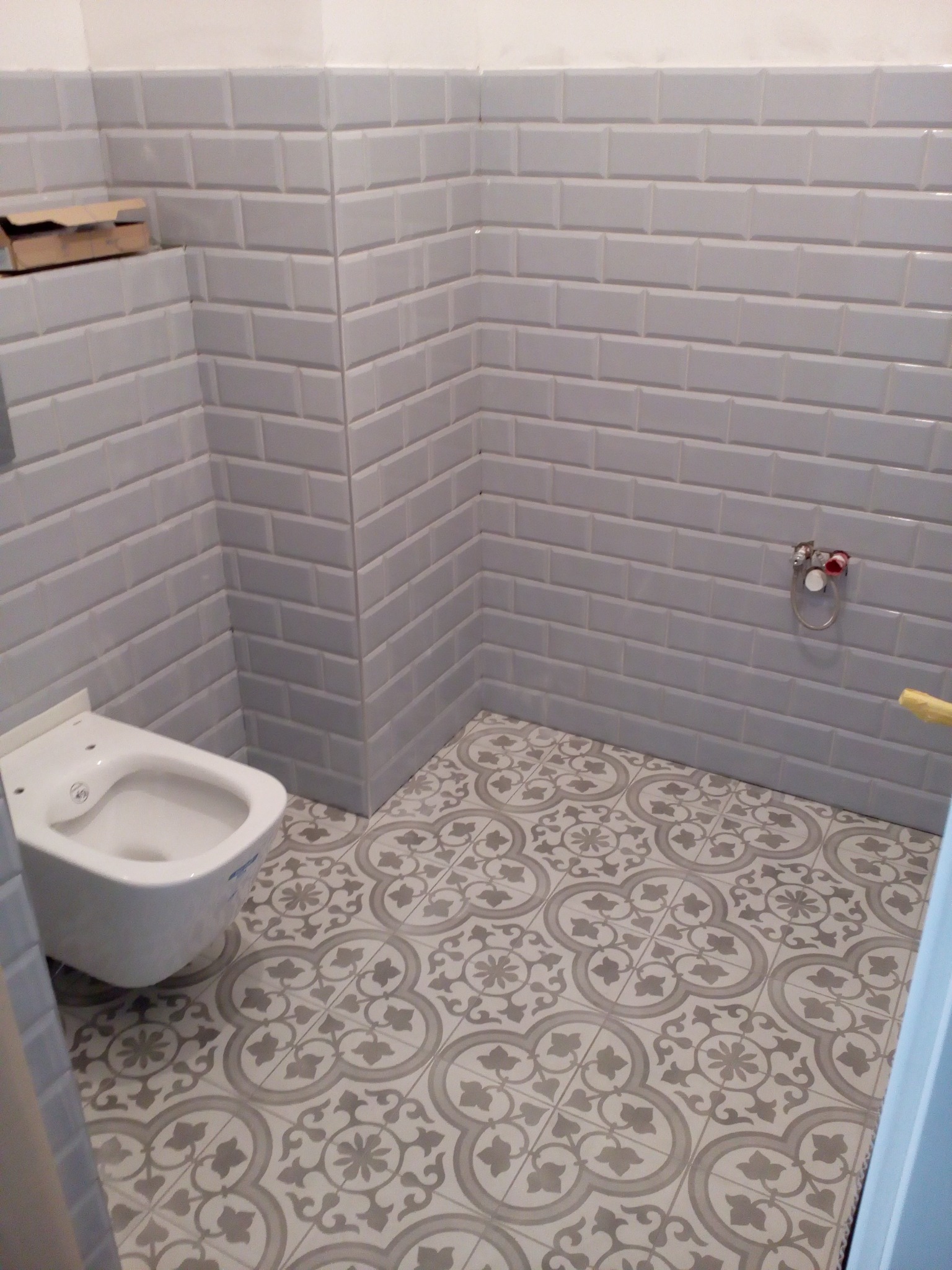 Wykończona łazienka w Chojnicach: szare płytki typu metro na ścianach, dekoracyjne płytki podłogowe w odcieniach szarości i bieli, wisząca toaleta.