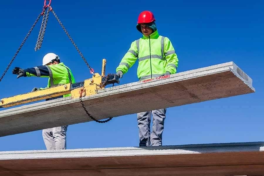 Montaż betonowego panelu stropowego w Bydgoszczy przy użyciu dźwigu, pracownicy w odblaskowych kurtkach i kaskach nadzorują proces.