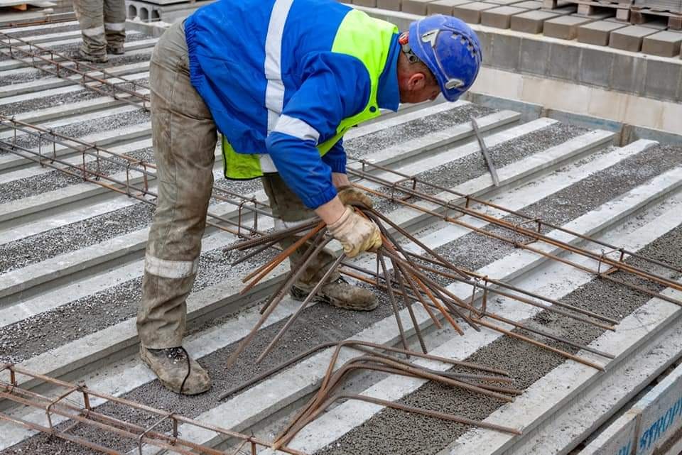 Pracownik w odzieży roboczej układa zbrojenie na prefabrykowanych płytach betonowych stropowych z wypełnieniem kruszywem.