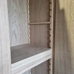 Wnętrze szafy z regulowanymi półkami, widoczne wycięcia na wsporniki, drewno w jasnym odcieniu dębu.