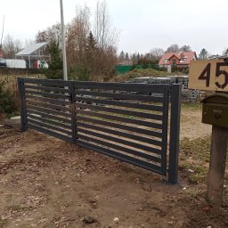 JOGILLA Art Welding - Nowoczesna, pozioma brama wjazdowa w kolorze grafitowym na tle posesji z widocznym numerem domu 45b i skrzynką pocztową.