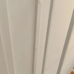 Kątowe ujęcie białej balustrady z metalowymi elementami mocującymi, widoczne fragmenty drewnianych schodów w tle.