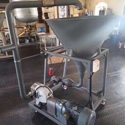 JOGILLA Art Welding - Kompletna instalacja przemysłowa z lejkiem zasypowym, pompą i silnikiem na mobilnej platformie, połączona rurami, z widocznymi elementami elektrycznymi i skrzynkami w tle.