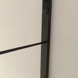 JOGILLA Art Welding - Fragment czarnej, metalowej balustrady z okrągłym mocowaniem na tle jasnej ściany, widoczne poziome pręty.