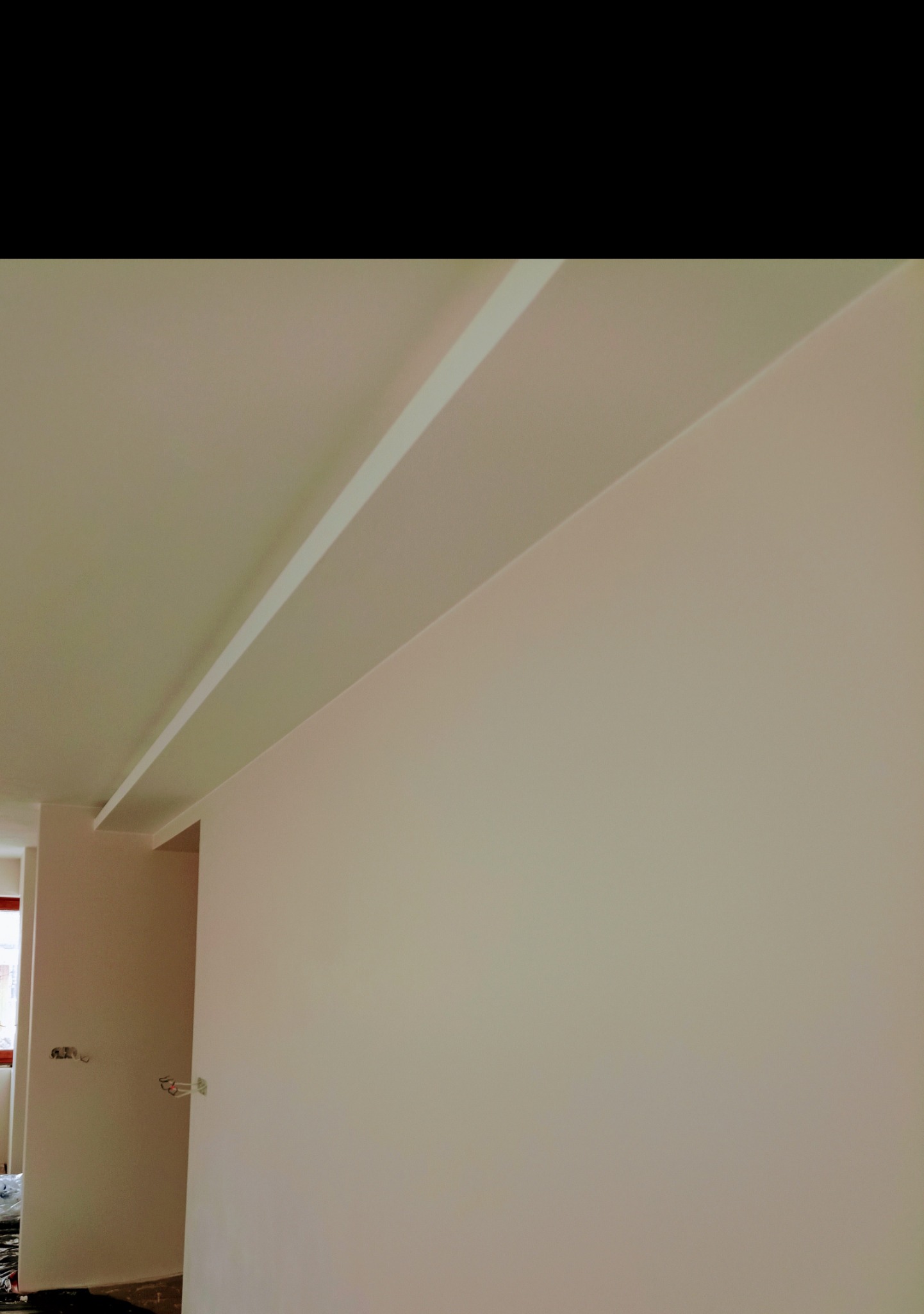 Świeżo pomalowana ściana w jasnym odcieniu z widoczną listwą przysufitową, widok z dołu, wnętrze w trakcie wykańczania.