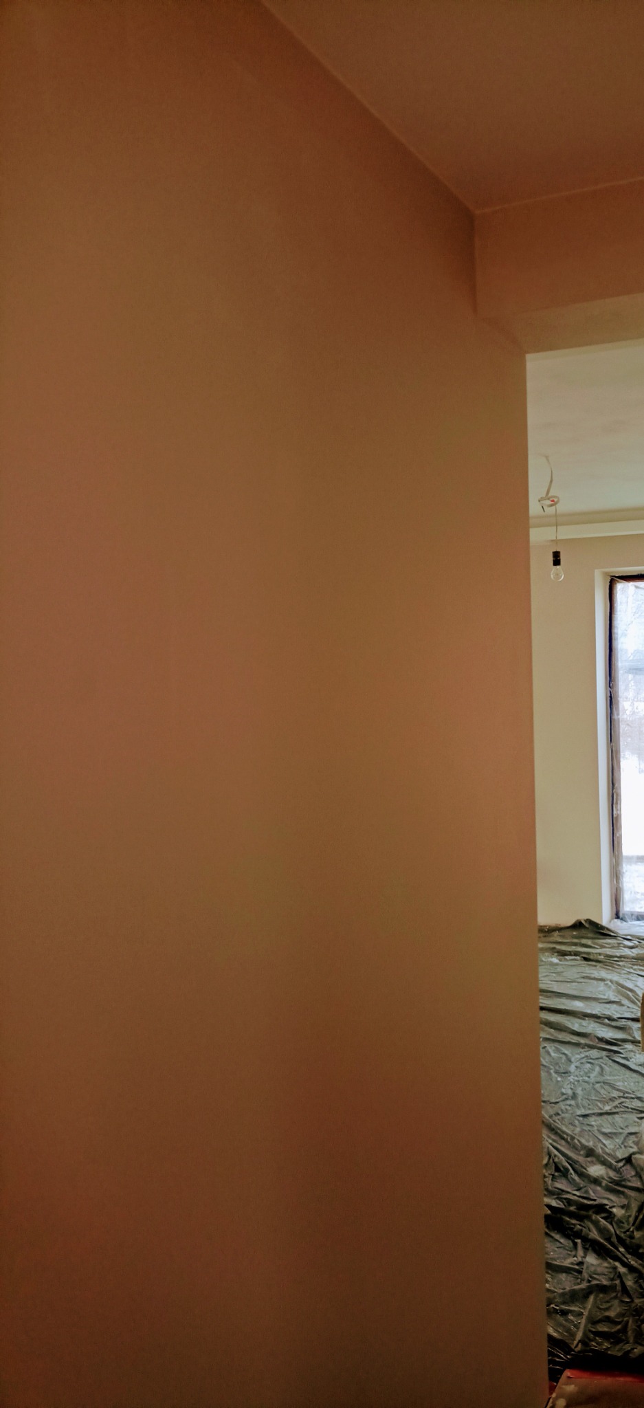 Świeżo wykończona ściana w odcieniu beżu, widoczna z bliska, z podłogą zabezpieczoną folią malarską w tle