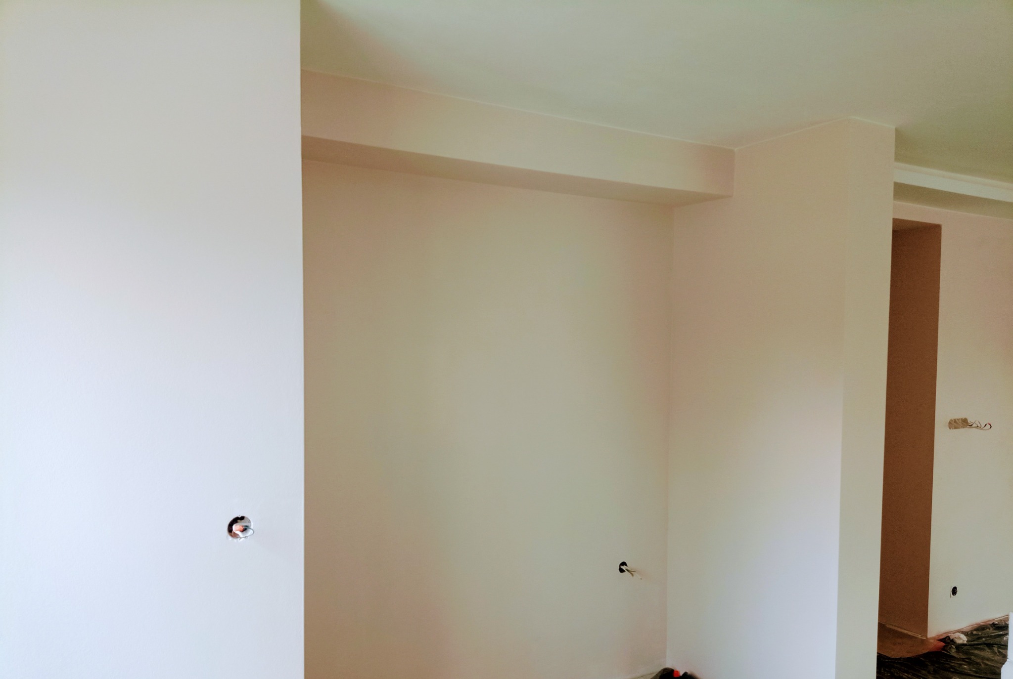 Wnętrze świeżo po pracach wykończeniowych w Mińsku Mazowieckim, ściany i sufit pomalowane na jasny odcień, widoczne otwory na gniazdka elektryczne i zabezpieczona folią podłoga.