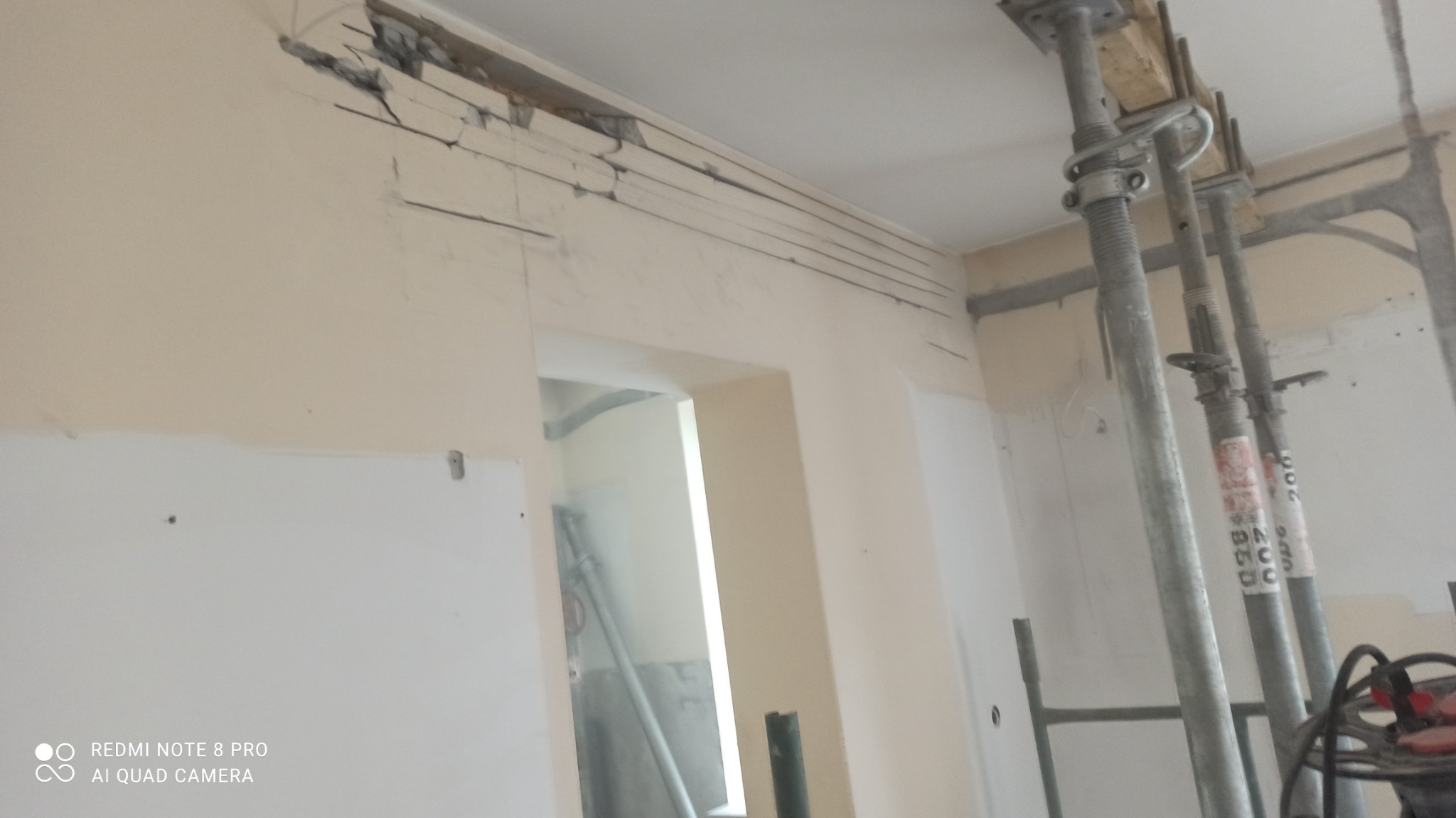 Fragment ściany z uszkodzeniami po demontażu, podparta metalowymi stemplami budowlanymi, widoczne ślady po cięciu i kruszeniu materiału.