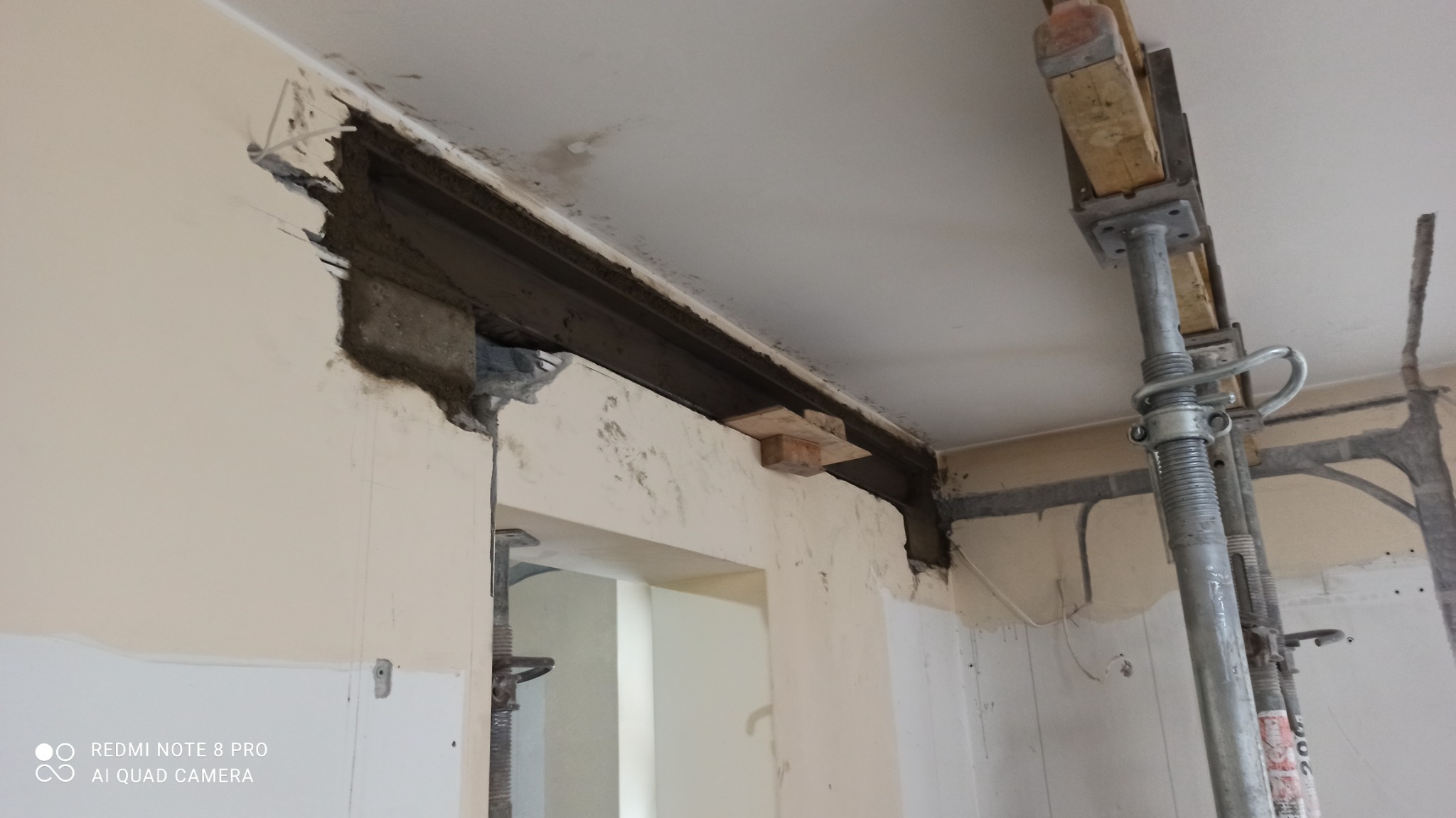 Wzmocnienie otworu w ścianie w Warszawie za pomocą stalowej belki i stempli budowlanych podczas prac wyburzeniowych.