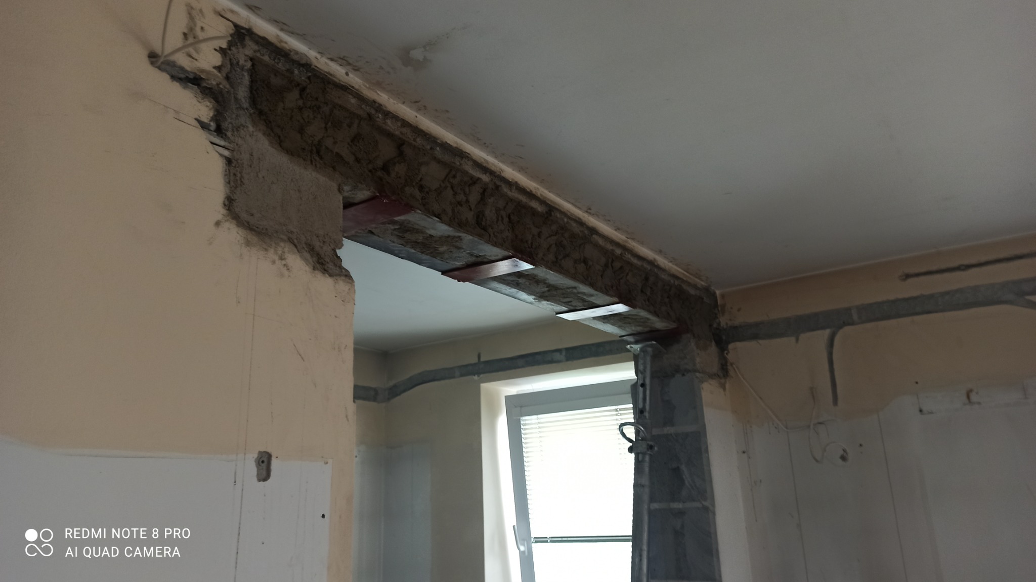 Otwór w ścianie po wyburzeniu, wzmocniony metalowymi elementami, widoczne ślady po kuciu i instalacjach.