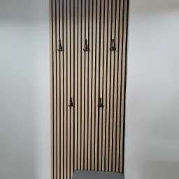 Panel ścienny z drewnianych listewek z czarnymi haczykami, widoczne buty sportowe i fragment szafki z siedziskiem.