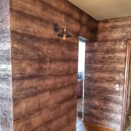 Wnętrze korytarza z panelami ściennymi imitującymi ciemne drewno, oświetlone lampą w stylu retro z żarówką Edisona, widok na sąsiednie pomieszczenie.