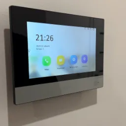 Panel dotykowy wideodomofonu Hikvision zamontowany na ścianie, wyświetlający godzinę, datę i ikony funkcji: Połącz, Wiadomość, Widok na żywo, Ustawienia.