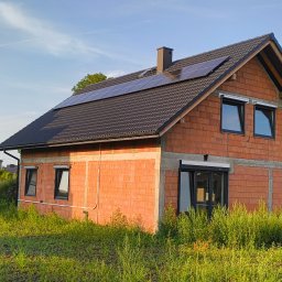 DMS System sp.z o.o. - Surowa bryła domu jednorodzinnego w trakcie budowy, z zamontowanymi panelami fotowoltaicznymi na dachu krytym czarną dachówką.