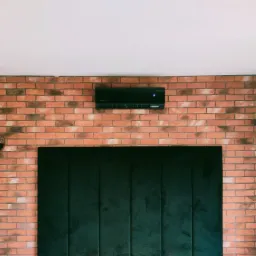 Czarny klimatyzator ścienny zamontowany na ceglanej ścianie z dwoma srebrnymi lampami kulistymi po bokach i ciemnozielonym panelem dekoracyjnym poniżej.