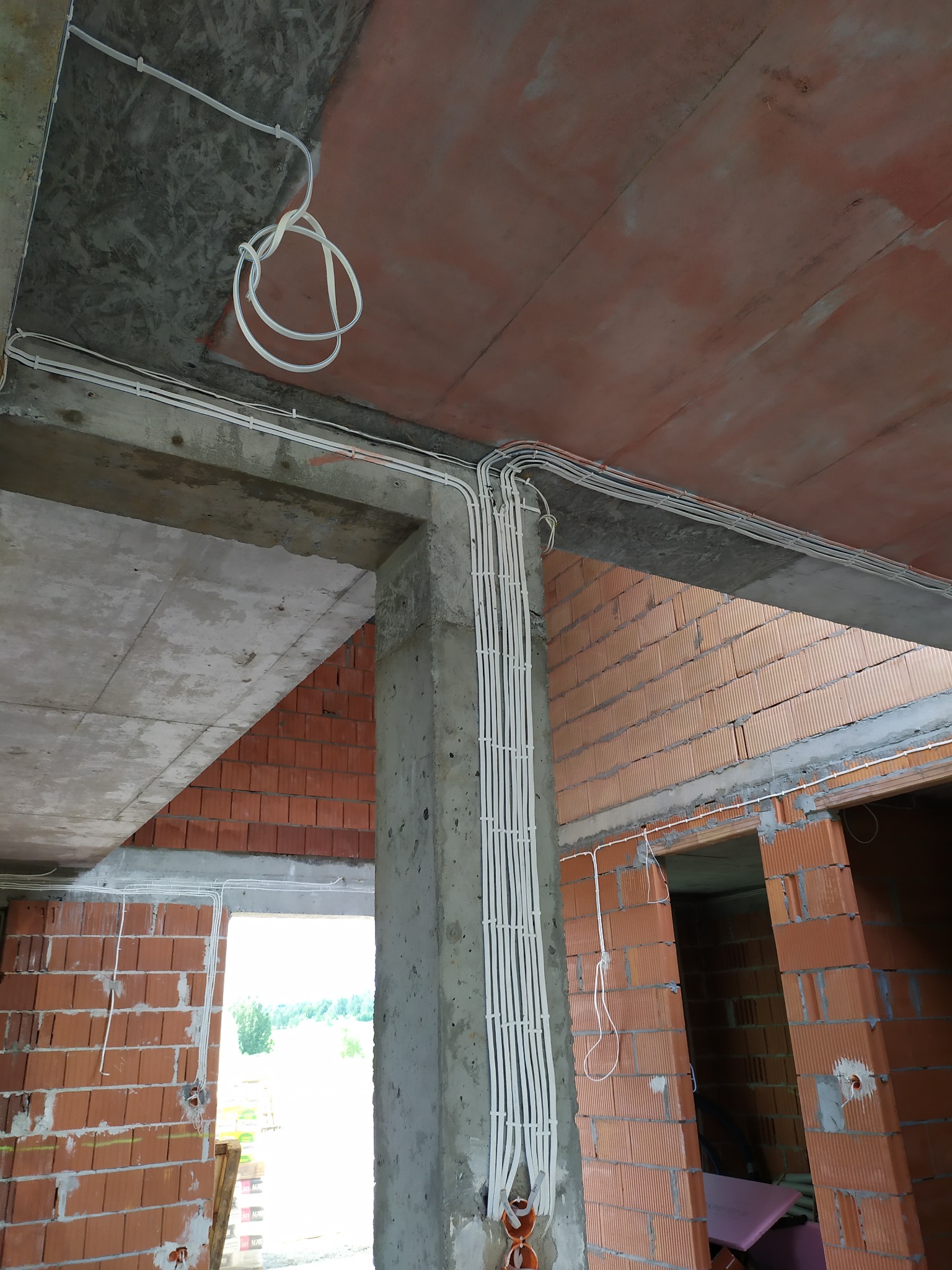 Białe kable elektryczne prowadzone po suficie i ścianach z czerwonej cegły w surowym wnętrzu budynku w Wadowicach, widoczne elementy konstrukcyjne z betonu.