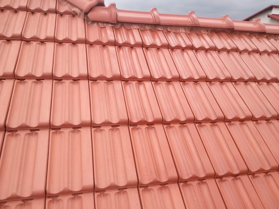 Czerwona dachówka ceramiczna ułożona na dachu, widoczna z bliska, z delikatnym połyskiem i widocznym fragmentem membrany dachowej.