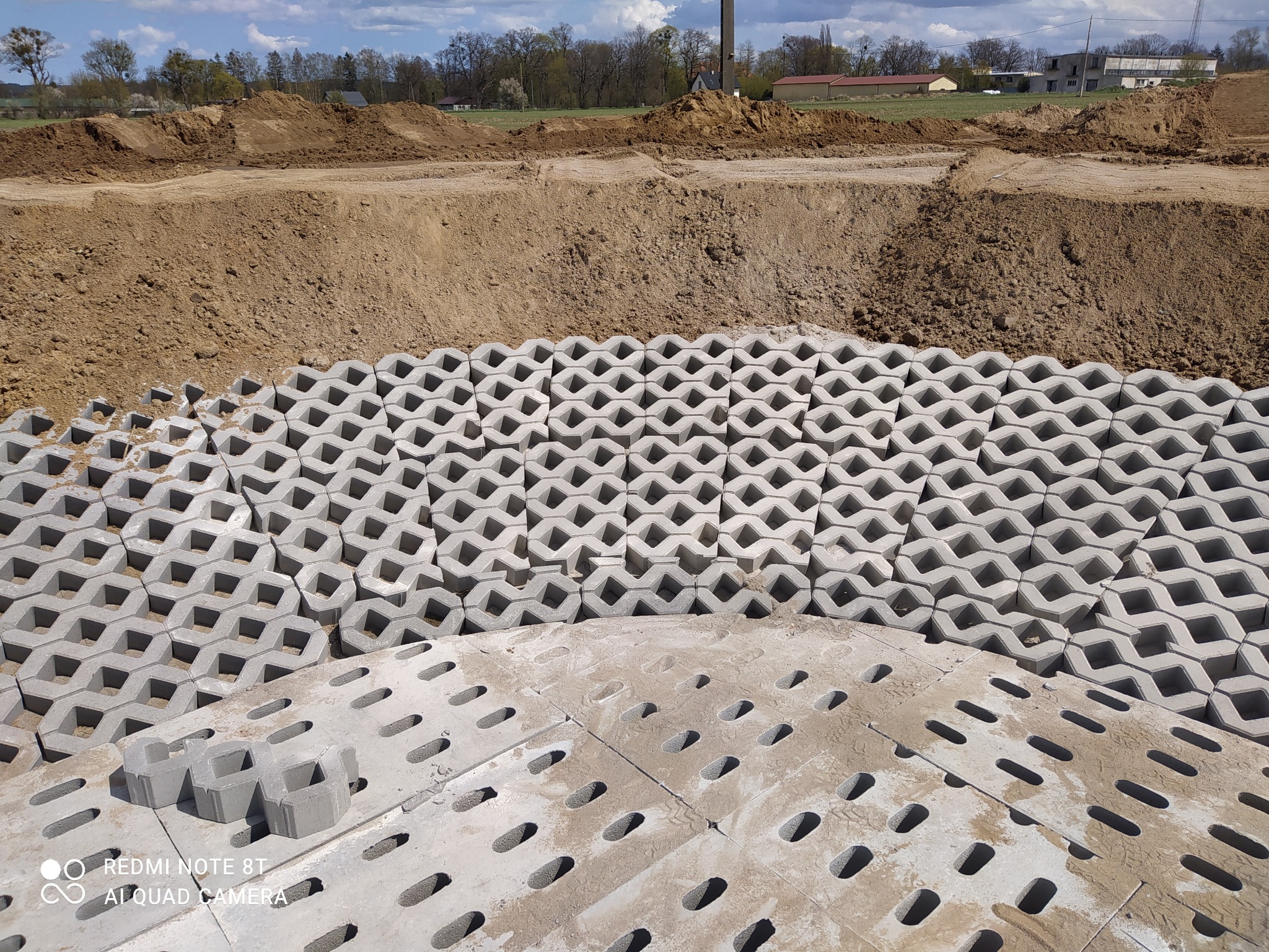 Przygotowanie podłoża pod nawierzchnię z ażurowych płyt betonowych i kostki brukowej na placu budowy, widoczne wykopaliska ziemne w tle.