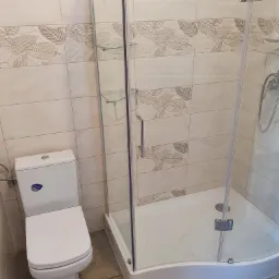 Wykończona łazienka z kabiną prysznicową z hartowanego szkła i toaletą Cersanit, płytki z motywem liści na ścianach.