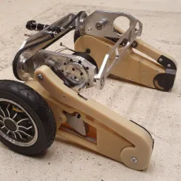 Nietypowy dwukołowy pojazd inżynieryjny z elementami z tworzywa i metalu, napędzany paskiem zębatym, widoczne detale konstrukcyjne.