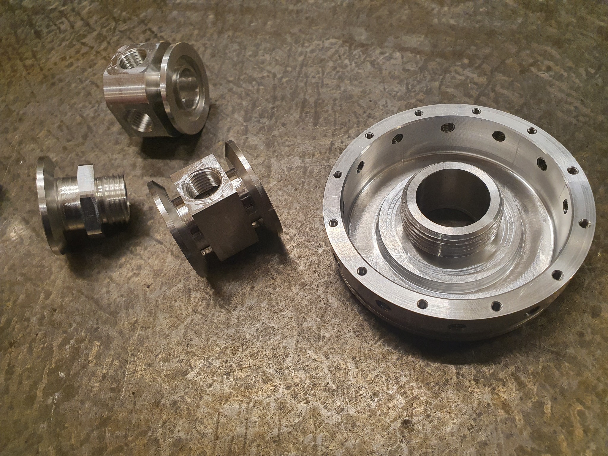 Precyzyjnie wykonane, metalowe elementy z gwintami i otworami, ułożone na szorstkiej, metalowej powierzchni z widocznymi śladami obróbki.