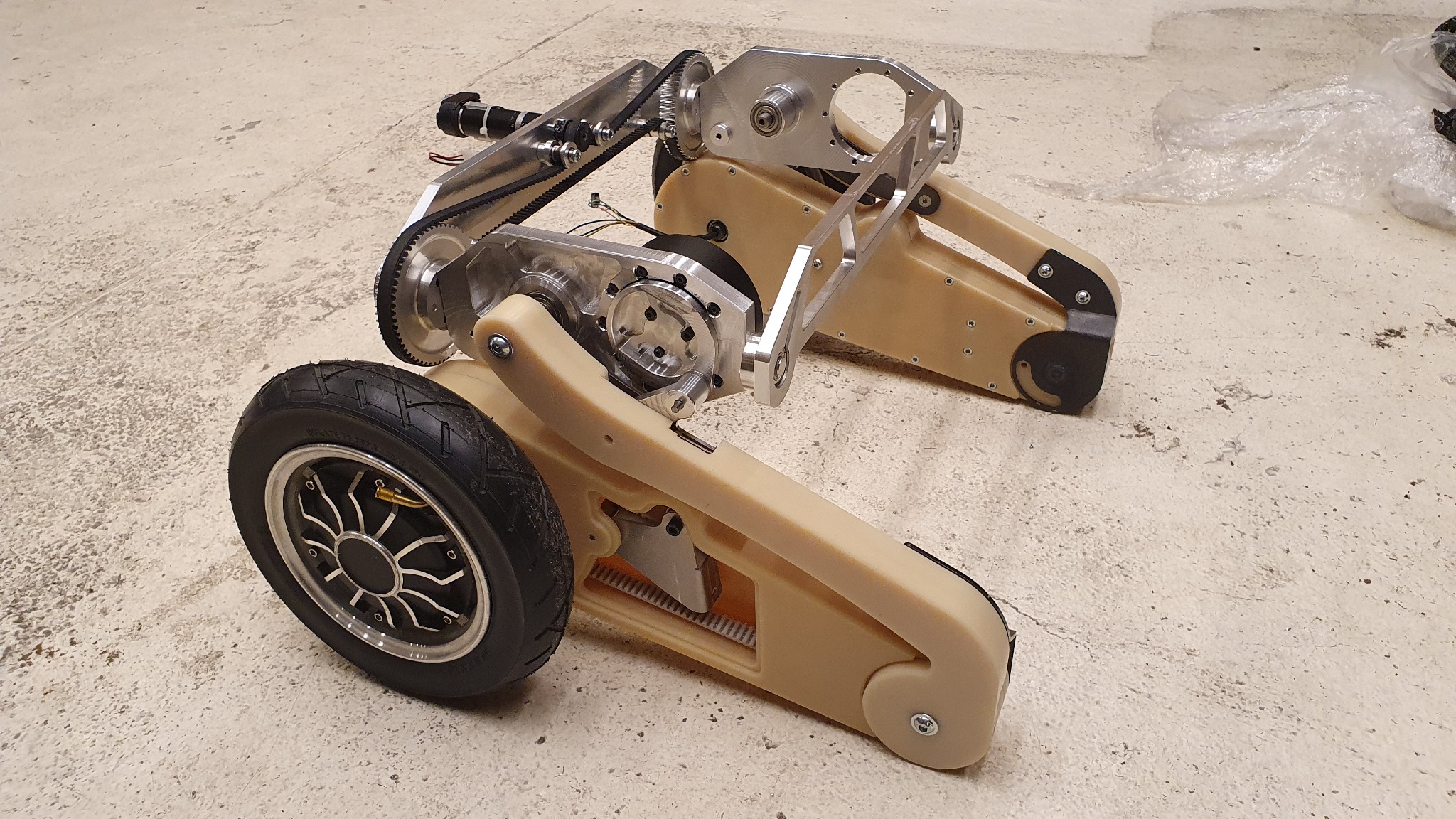 Nietypowy dwukołowy pojazd inżynieryjny z elementami z tworzywa i metalu, napędzany paskiem zębatym, widoczne detale konstrukcyjne.