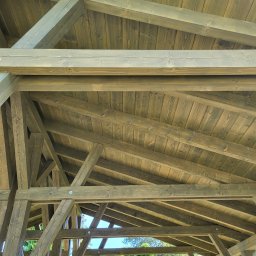 Firma Remontowo-Budowlana Pilch Robert - Konstrukcja drewnianej altany z widocznym dachem z desek, impregnowana na zielono-szary odcień, z widocznym ogrodem w tle, uchwycona z perspektywy żabiej.