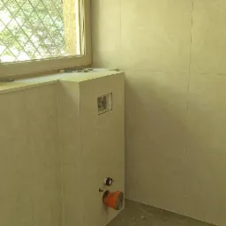 Wykończona łazienka z zamontowaną instalacją podtynkową WC na tle okna z ozdobną kratą. Widoczne płytki ceramiczne w odcieniach beżu i szarości.