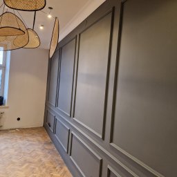 Firma Remontowo-Budowlana Pilch Robert - Ściana z dekoracyjnymi panelami w kolorze szarości, widoczna pod kątem, z drewnianą podłogą w jodełkę i nowoczesną lampą. Wykończenie wnętrza w stylu klasycznym.