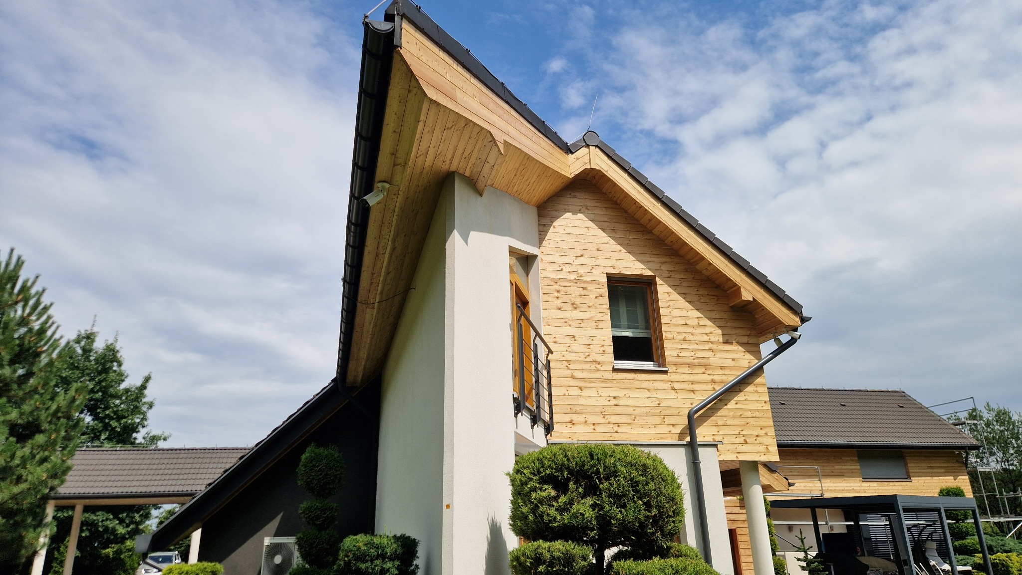 Nowoczesny dom z drewnianą elewacją i białym elementem architektonicznym, widok z dołu na tle błękitnego nieba.