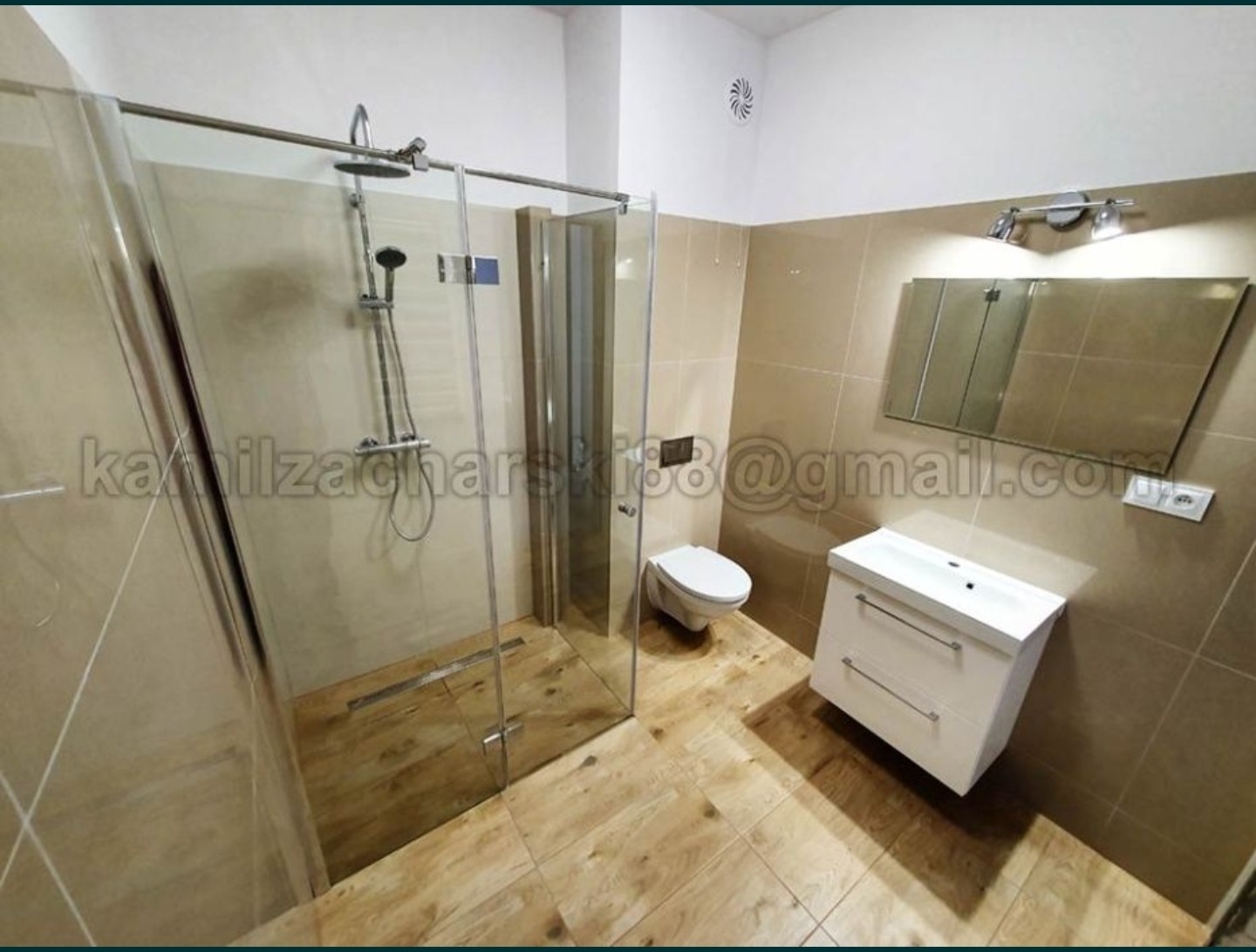 Nowoczesna łazienka w beżowych odcieniach z kabiną prysznicową typu walk-in, drewnopodobną podłogą, wiszącą toaletą i białą szafką z umywalką.