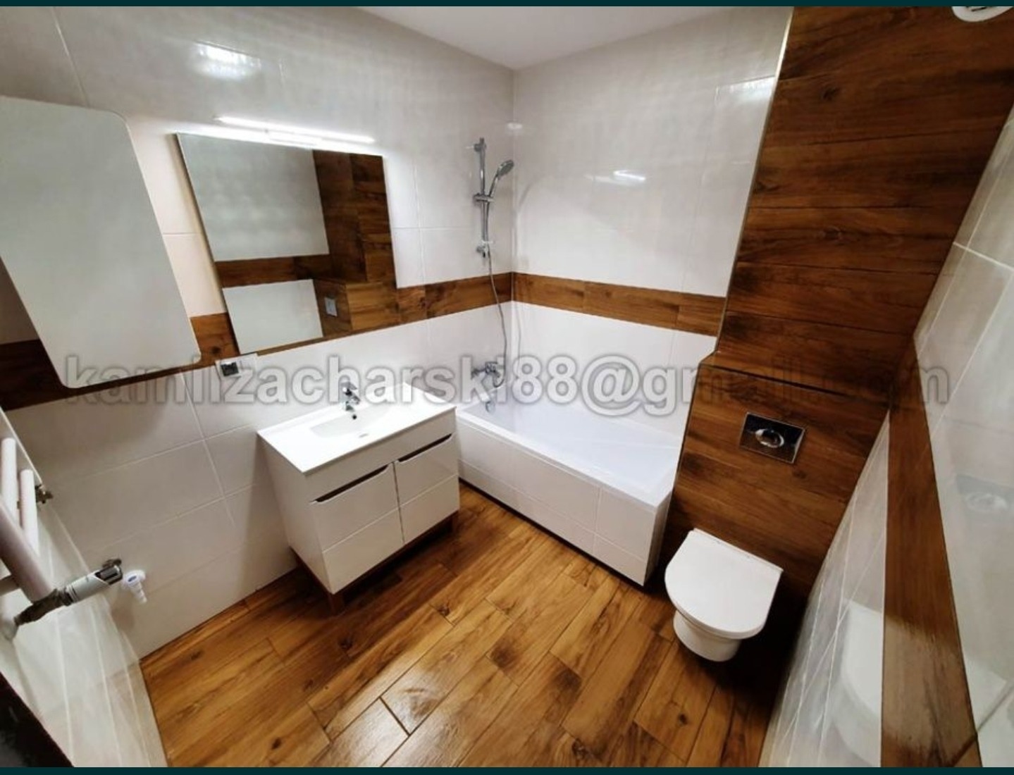 Nowoczesna łazienka z białymi płytkami, drewnopodobną zabudową, białą armaturą i podłogą z paneli imitujących drewno, widok z góry.