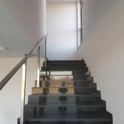 Nowoczesne, czarne schody z polerowanego kamienia z metalową balustradą w jasnym wnętrzu biurowym, widoczne odbicie sylwetki w powierzchni stopni.