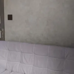 Szara, dekoracyjna ściana z efektem betonu w pokoju, widoczny fragment sofy, drzwi wewnętrzne z przeszkleniami i zasłona z wzorem marmuru.