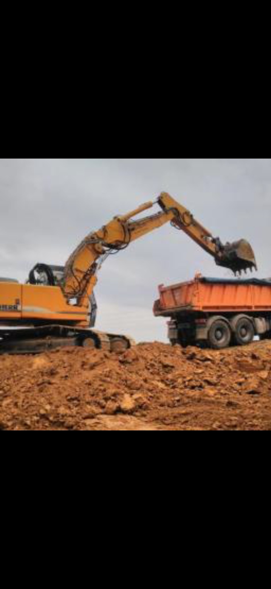 Żółta koparka Liebherr ładuje ziemię do pomarańczowej ciężarówki na tle pochmurnego nieba.