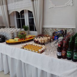 Firma Usługowa Finezja - Stół cateringowy z dekoracją z arbuza, paterami owoców, ciastami w pucharkach, napojami w butelkach i kartonikach, oraz stosem filiżanek do kawy, przygotowany na imprezę.