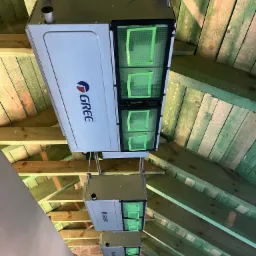 Kaskadowo zamontowane jednostki rekuperacyjne marki GREE w przestrzeni poddasza z widoczną drewnianą konstrukcją dachu.