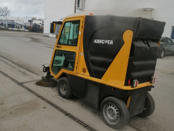 Żółto-czarna zamiatarka Karcher w trakcie pracy, zbierająca zanieczyszczenia z betonowej nawierzchni z kratką odpływową.