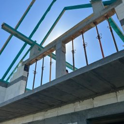 Usługi ogólnobudowlane Adaś - Wznoszenie domu z betonu komórkowego: widok na konstrukcję stropu i zbrojenie, podpory stalowe podtrzymujące szalunek, fragment więźby dachowej w tle.